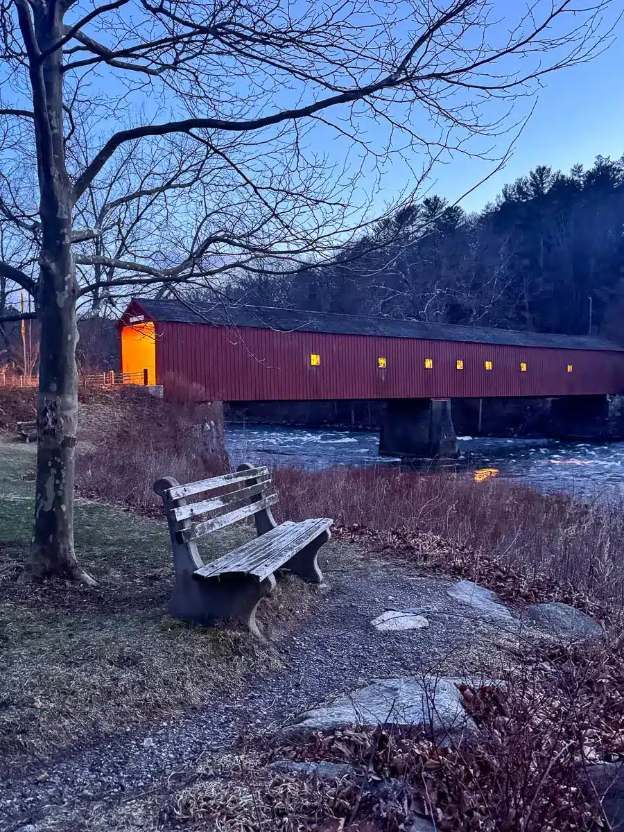 red covered bridge over river at dusk with golden light glowing through the windows along the bridge