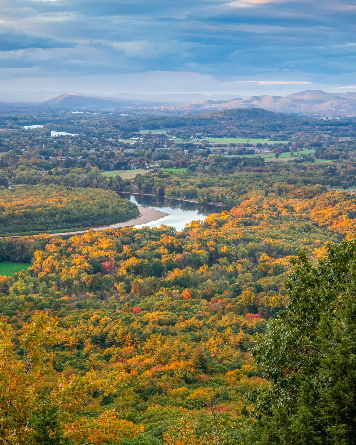 shimmering river in the distance surrounded by orange and green leaves on a fall hike in Massachusetts.
