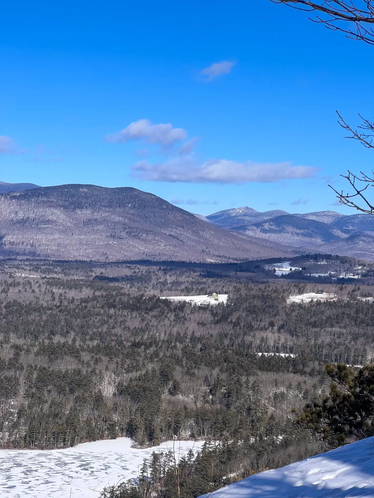 snowy lookout from a hike in new hampshire with frozen white lake below and bare brown mountains dusted with snow in the distance.