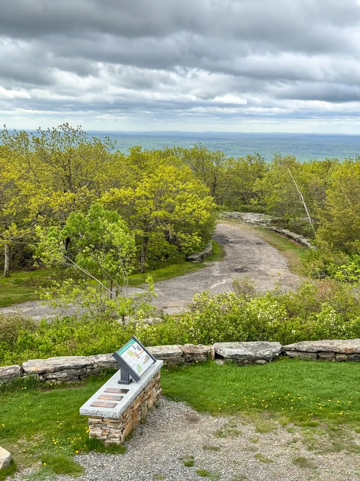 view from mount wachusett with rolling green hills and trees in the distance and gray cloudy sky.