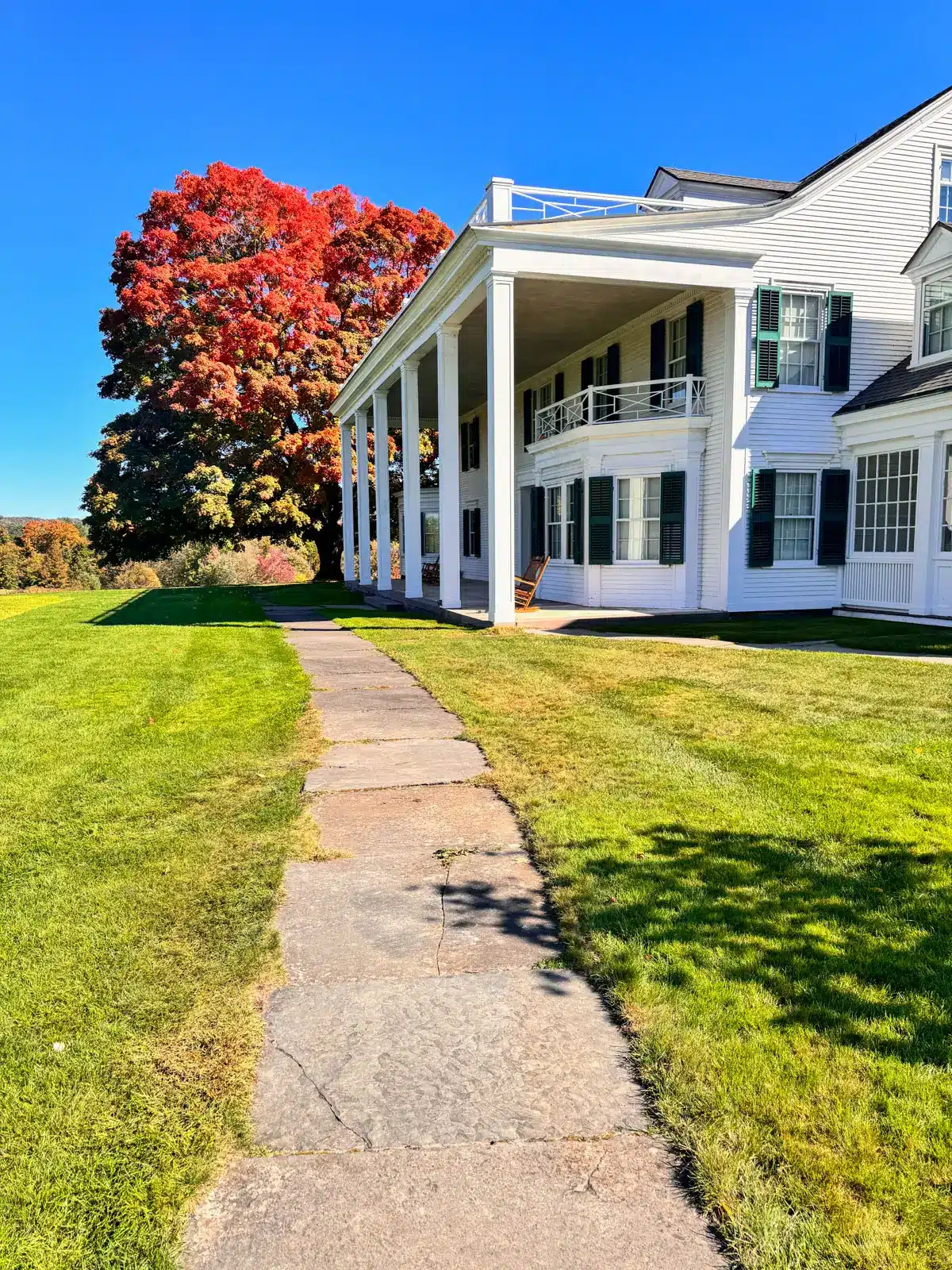 hill-stead museum with big white colonial and sidewalk and white fence surrounded by orange and yellow leaved trees.