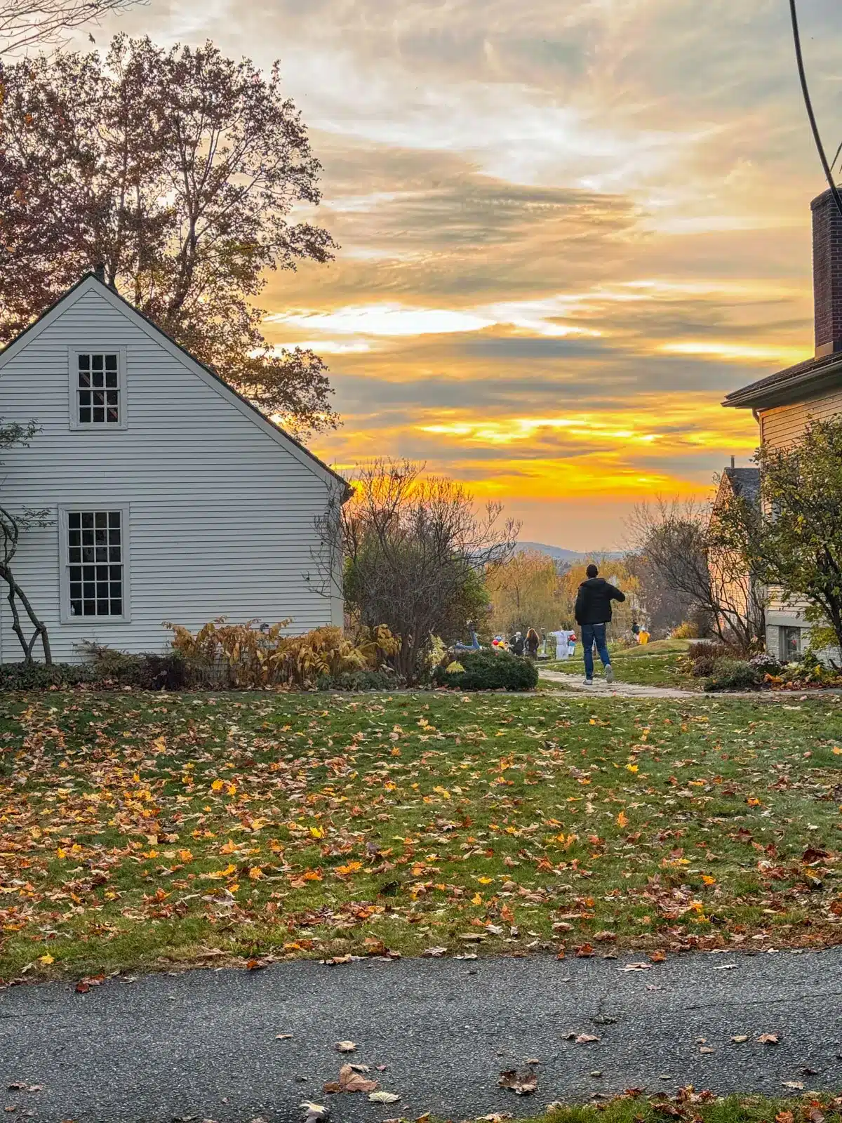 lawn and white colonial house at sunset with golden glow in the sky.