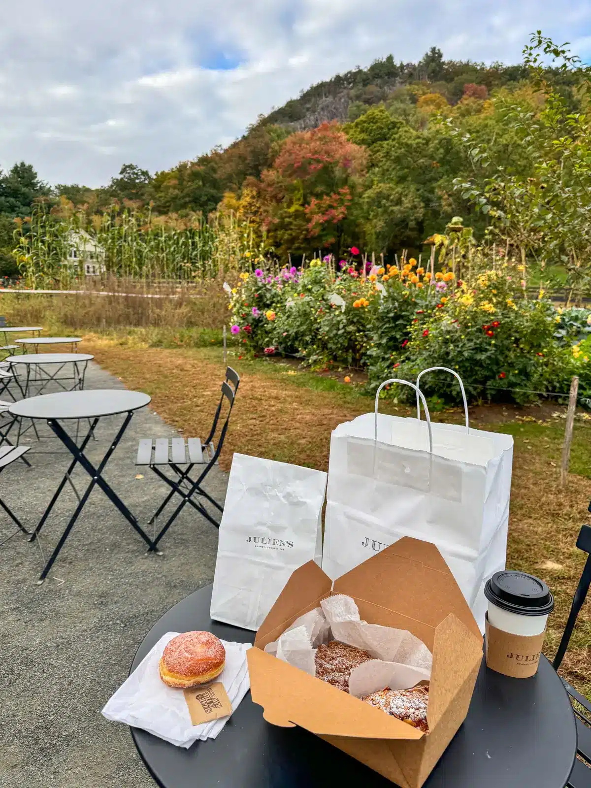 outside of juliens farmstore in granby with black two top tables and baked goods on table.