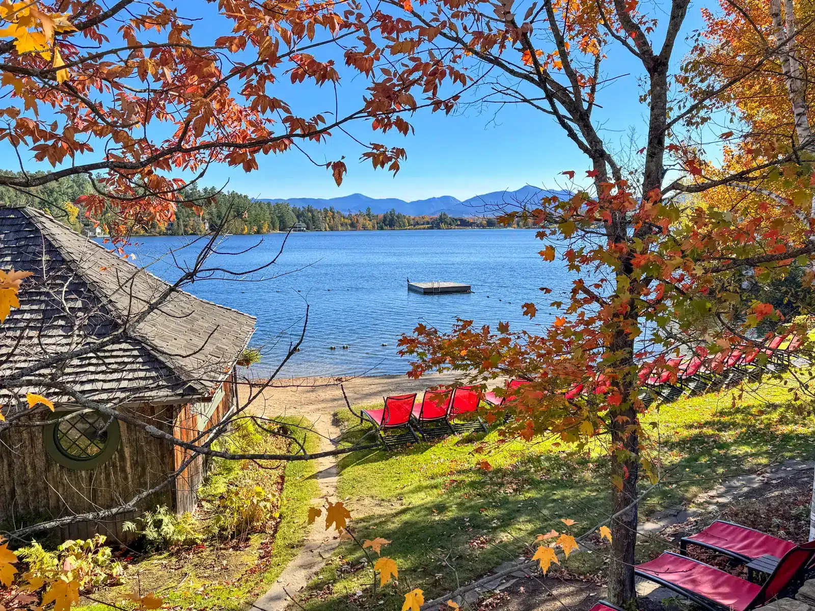 Mirror Lake in Lake Placid with blue water with red chairs in front of the water and lined with orange trees.