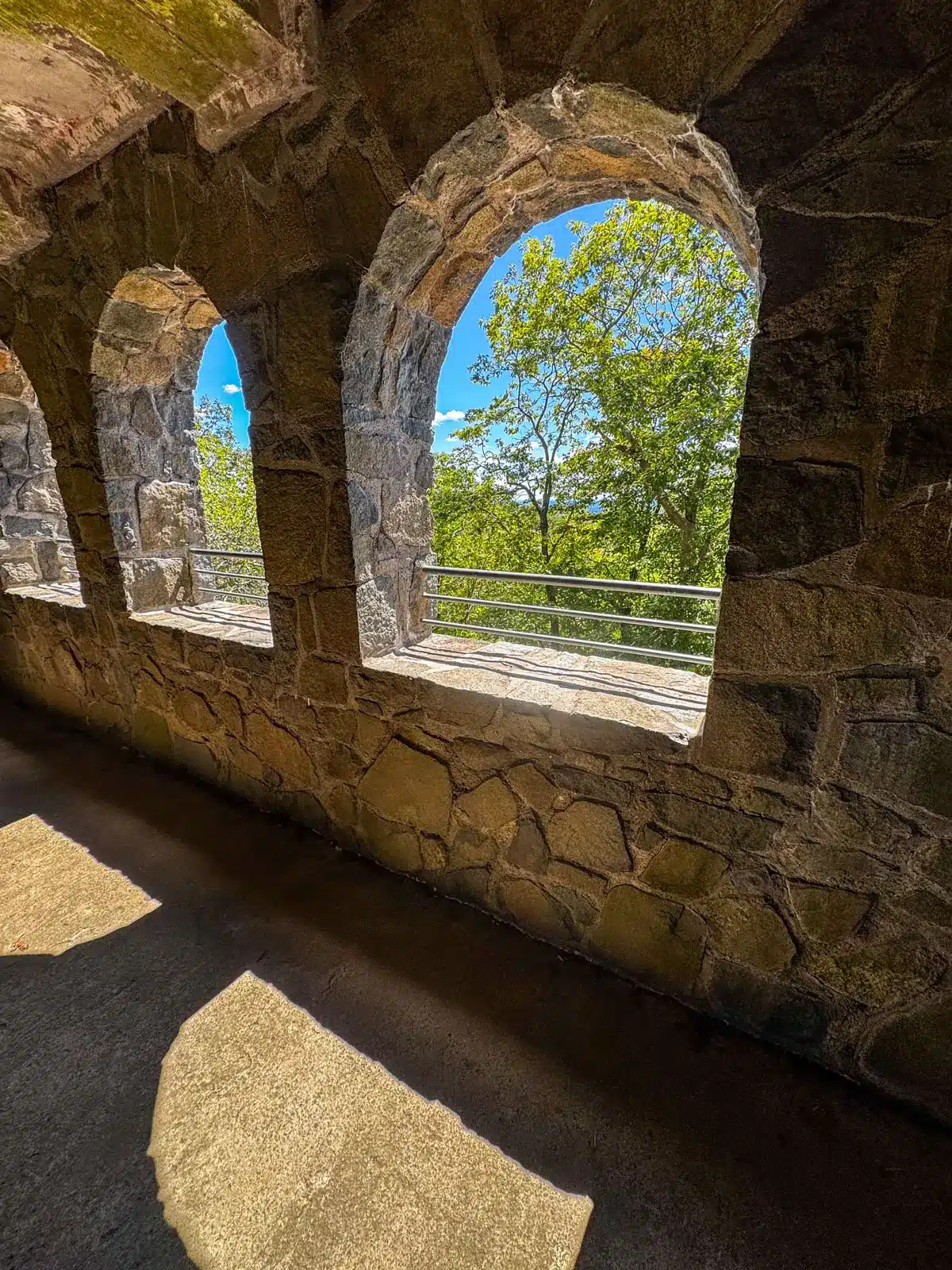 view from a round winder at the top of sleeping giant tower in hamden with rolling green landscape in the distance and blue skies above.