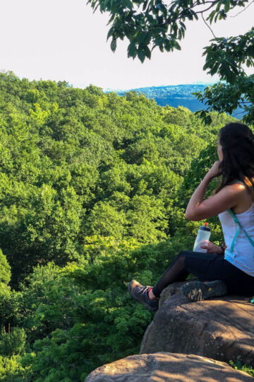 woman sitting on cliff ledge on top of sleeping giant state park in connecticut.