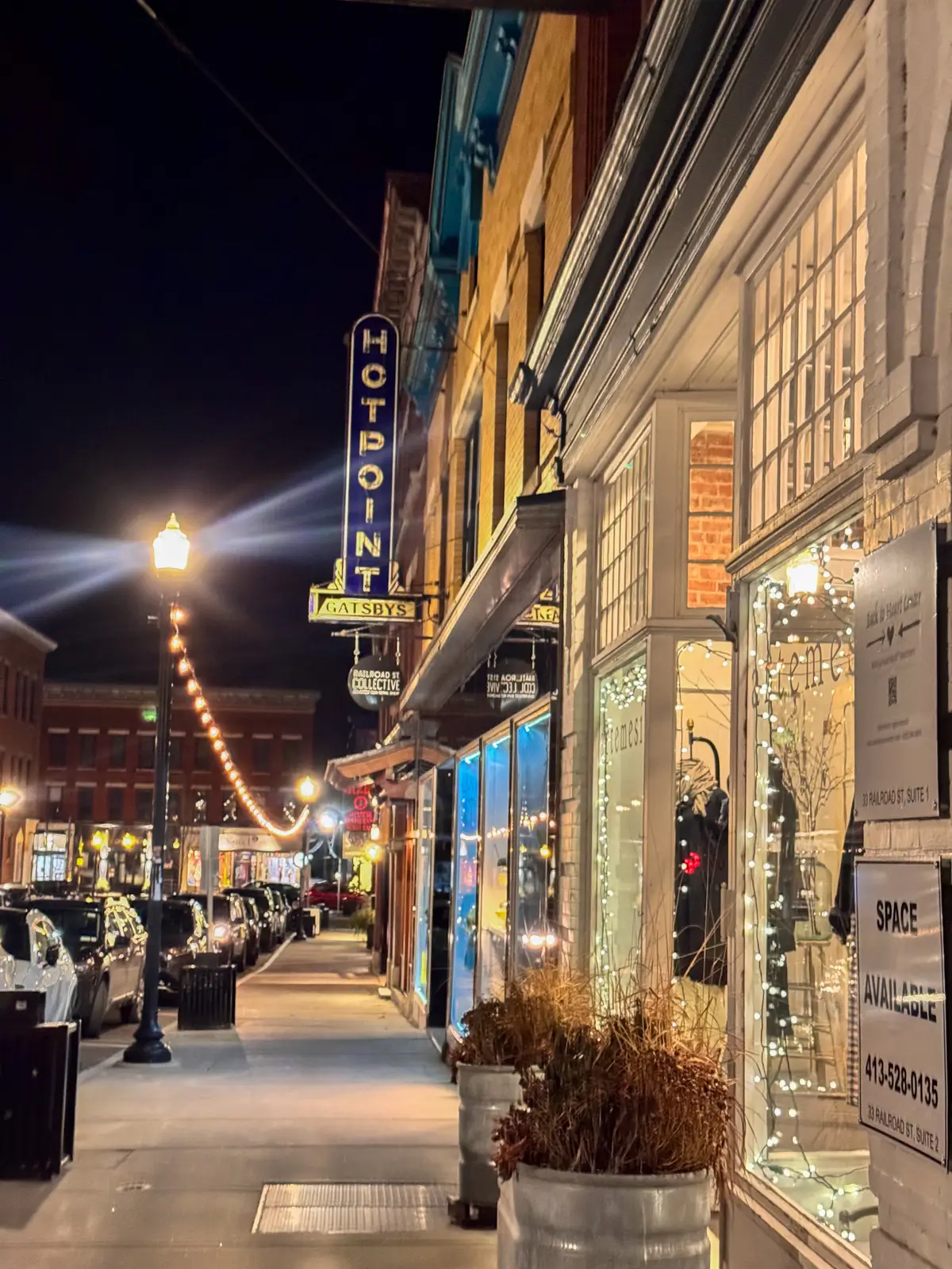 downtown great barrington at night with storefronts lit up from inside and sidewalk in front of stores.