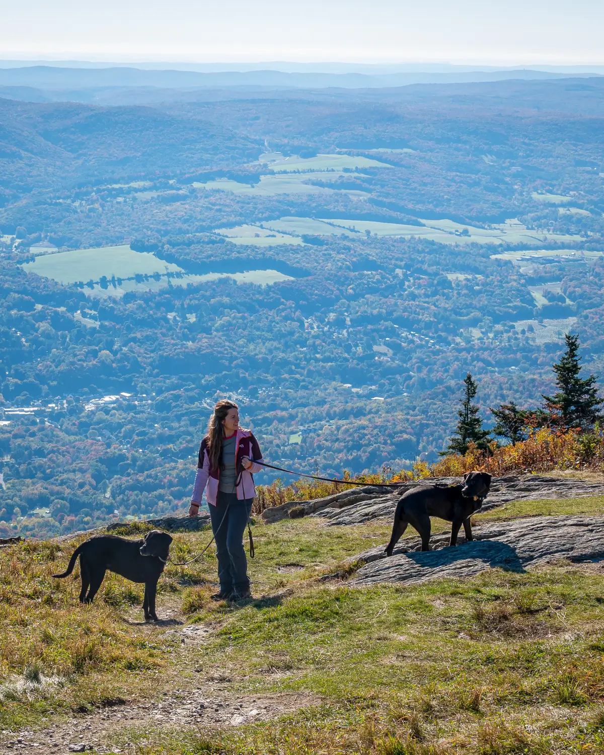 woman smiling at top of mountain with rolling green mountains in background at mount greylock in the berkshires.