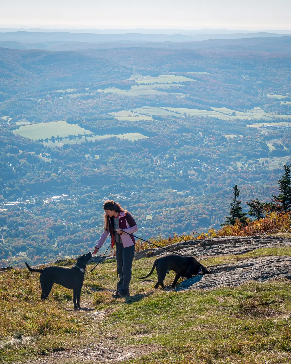 woman smiling at top of mountain with rolling green mountains in background at mount greylock in the berkshires.