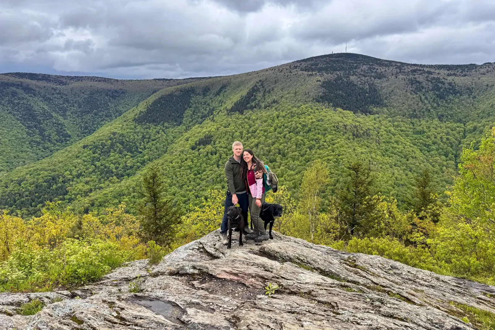 man and woman smiling at top of mountain with rolling green mountains in background in adams, massachusetts.