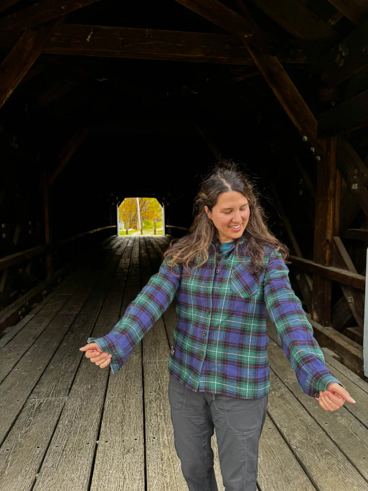 woman with brown hair smiling with forest green and dark blue plaid long sleeve flannel on.