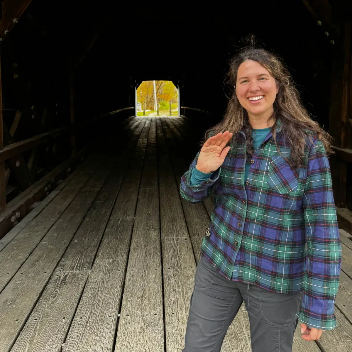 woman with brown hair smiling with forest green and dark blue plaid long sleeve flannel on.
