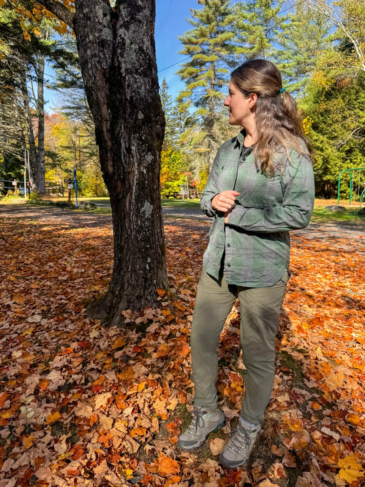brunette woman smiling at the camera on a fall day in vermont wearing an a gray and green light REI flannel shirt.