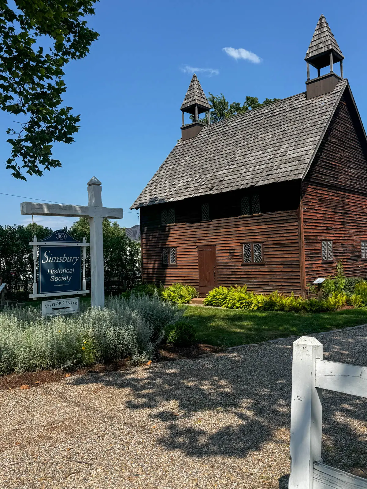 old brown cape with "simsbury historical society" blue sign in front and blue sky above.