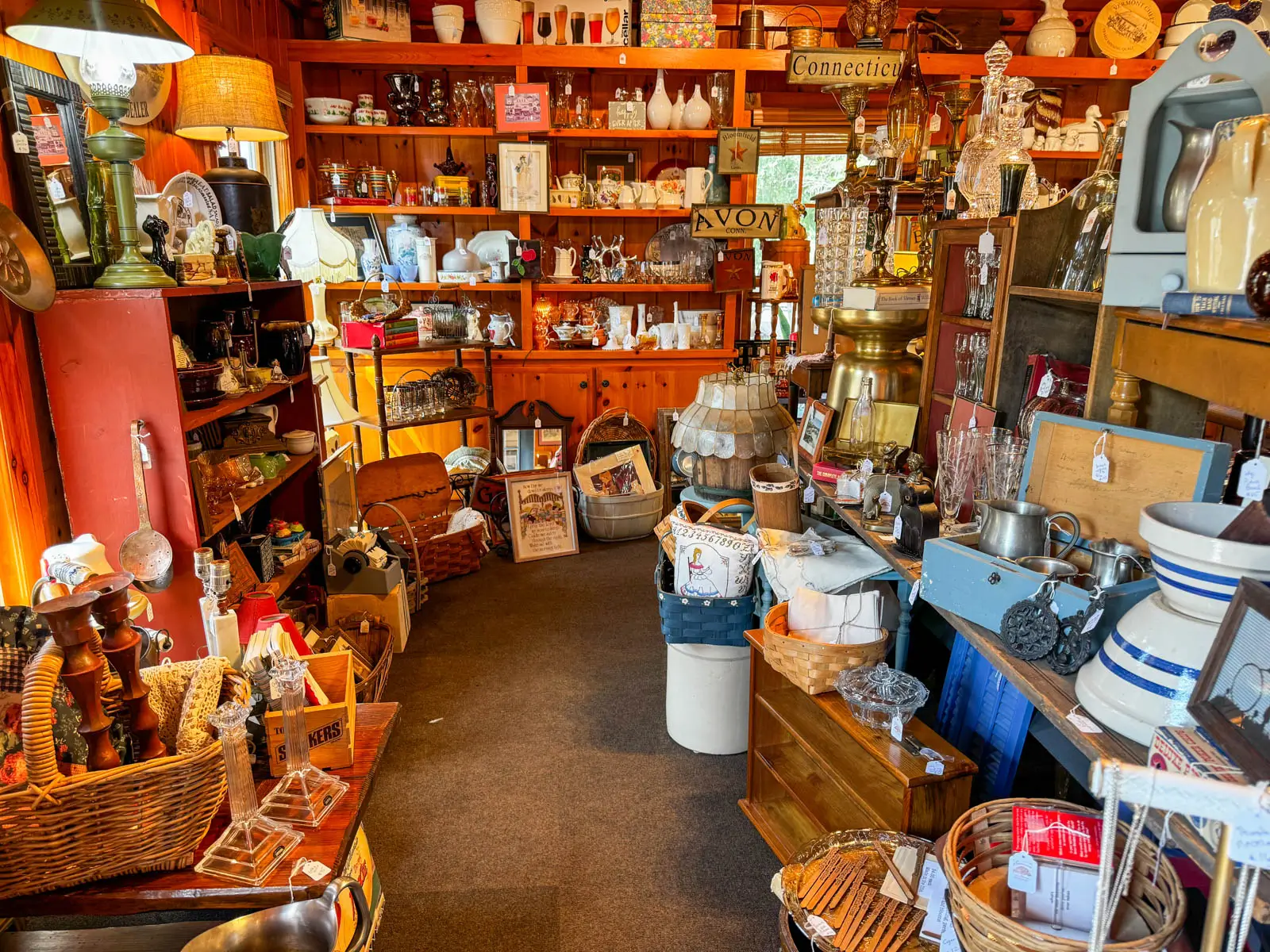 inside an antique shop with shelves of items and tables piled high with candlesticks, baskets, vases, glasses, and other items for sale.