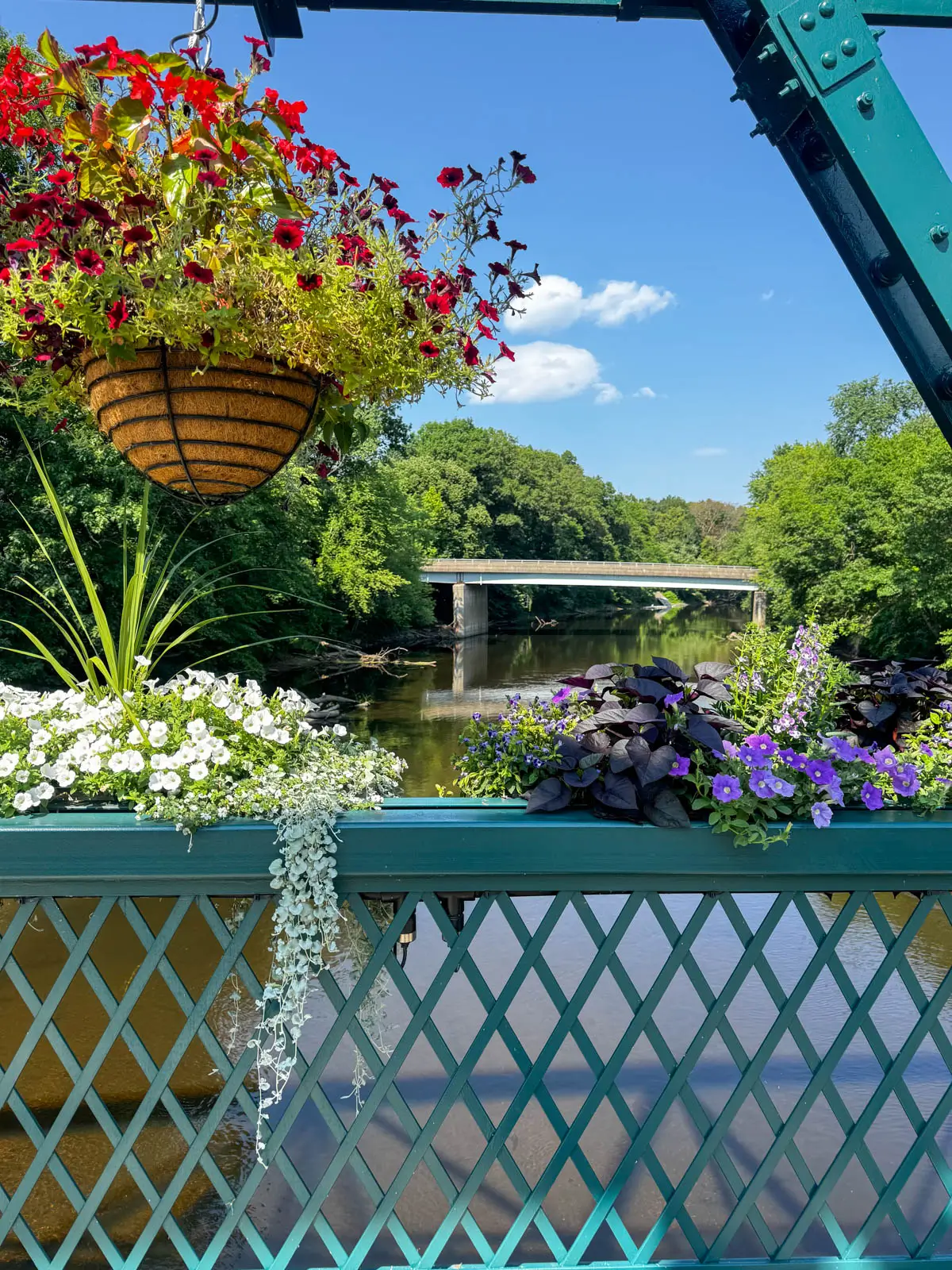 view from a green wrought iron bridge with red flower pot hanging and purple flower boxes lining the bridge.