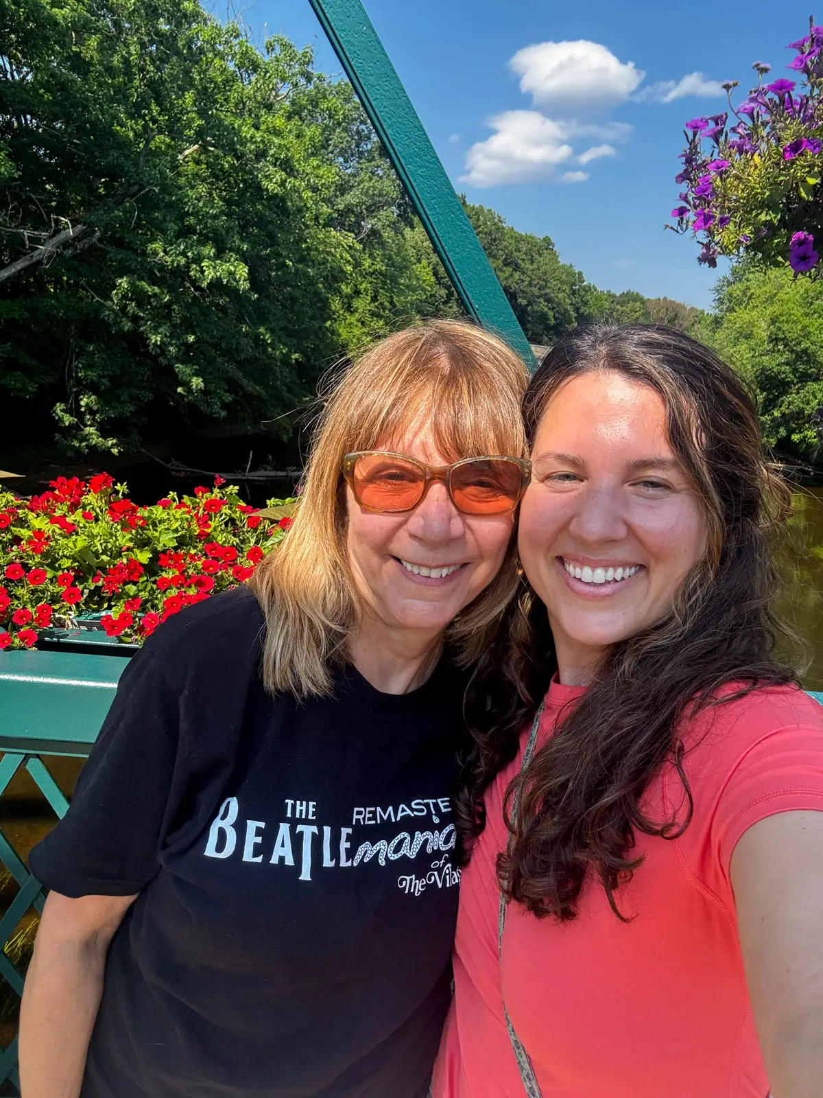 brunette woman smiling in coral colored shirt taking a selfie with older woman on left of her smiling with short blonde hair and a black t-shirt.