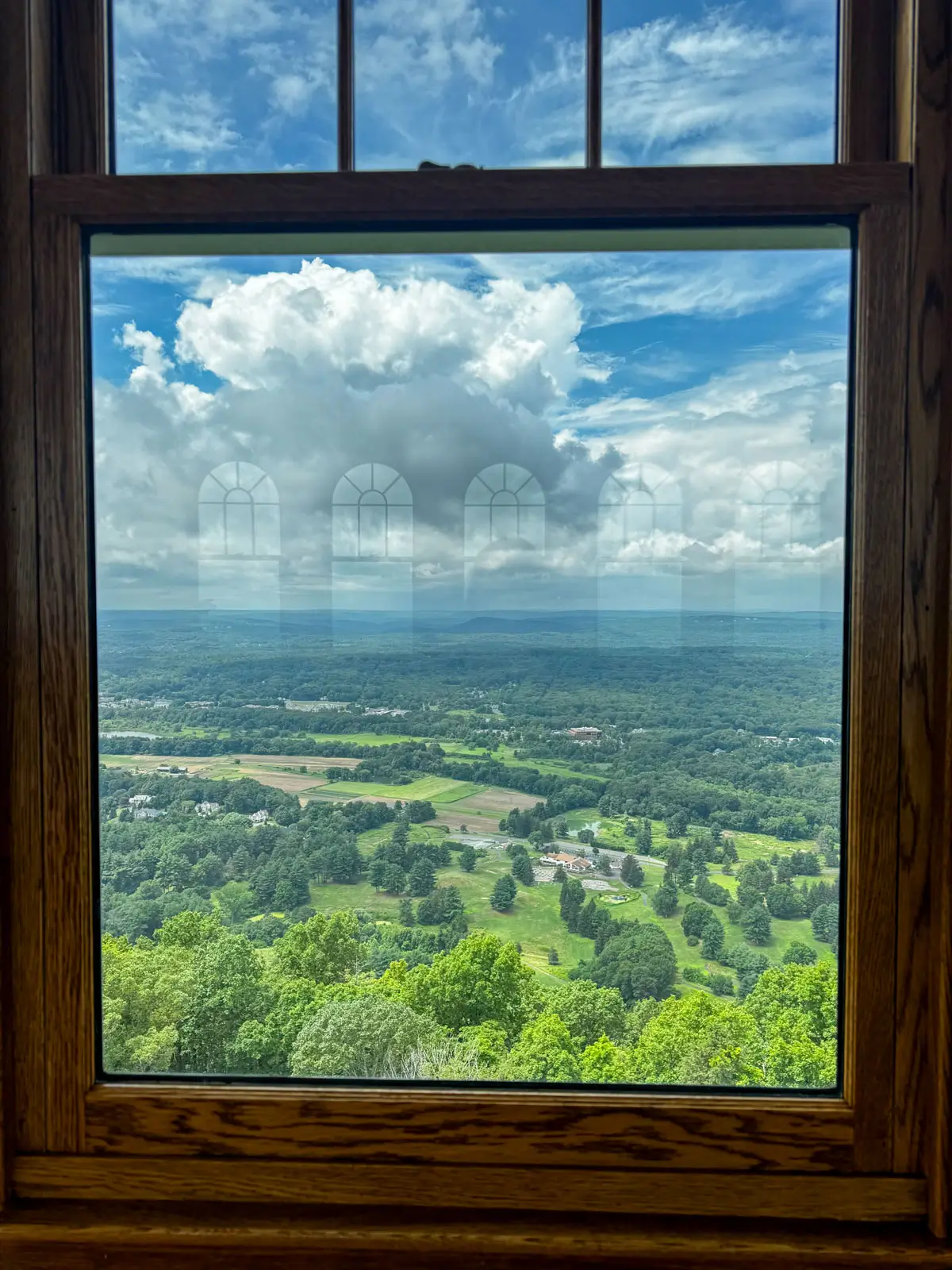 window view from the inside of heublein tower in simsbury connecticut with green farms and meadows and blue sky with fluffy clouds in the distance.