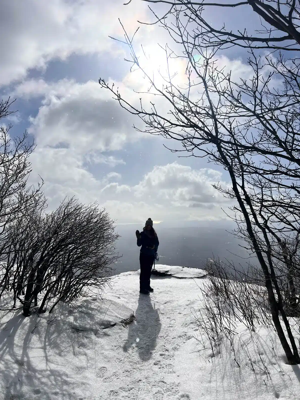silhouette of a women on top of overlook mountain in new york on a winter day with snow on the ground and fluffly white clowds in the sky.