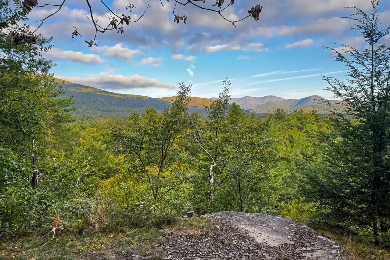 view from ashokan quarry hike in woodstock with views of mountain range on summer morning with bright green trees in front of the mountains and blue skies above.