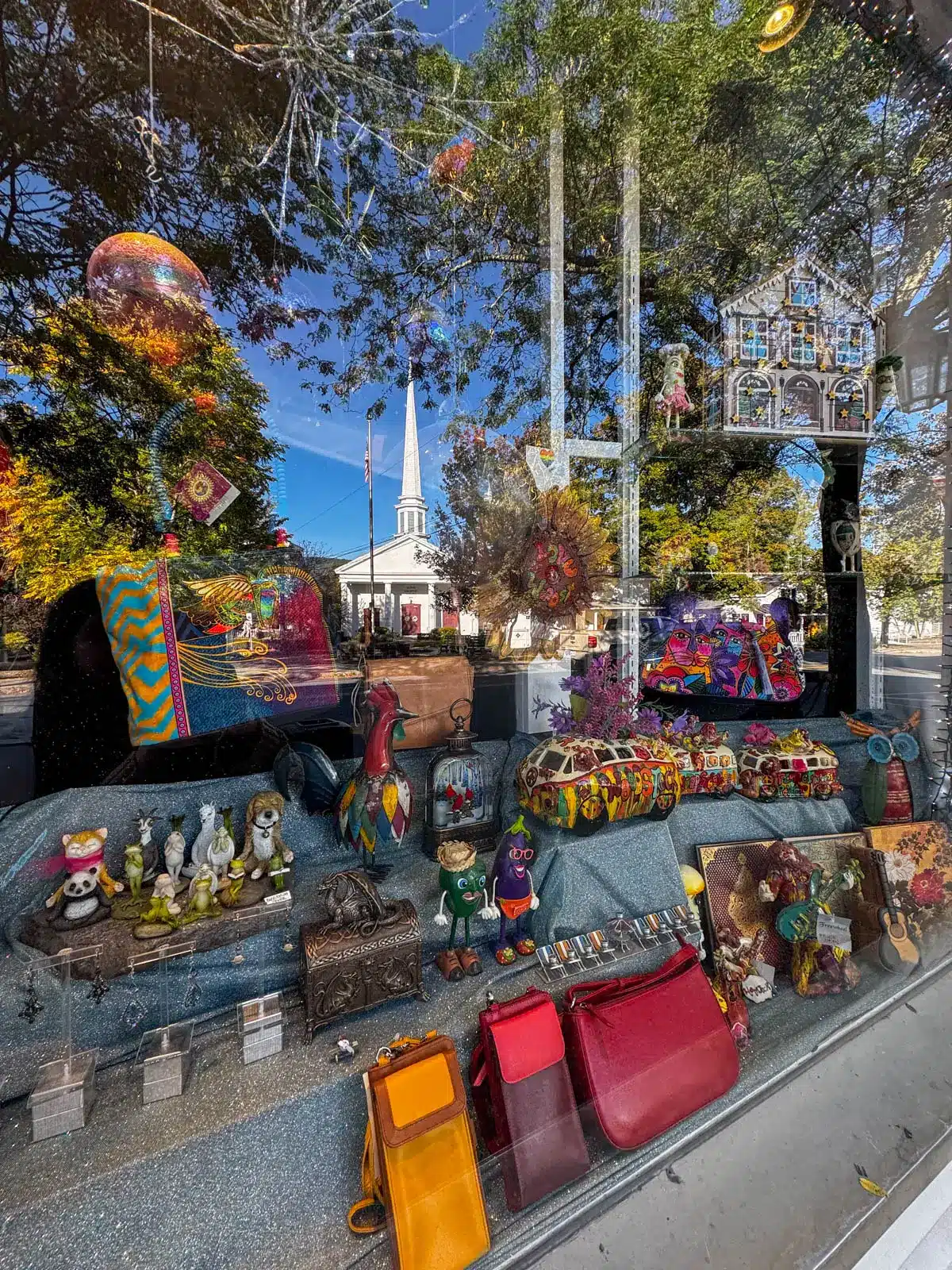 reflection in a shop along main street in woodstock new york with colorful items in the shop and reflection of white steeple church in woodstock ny.
