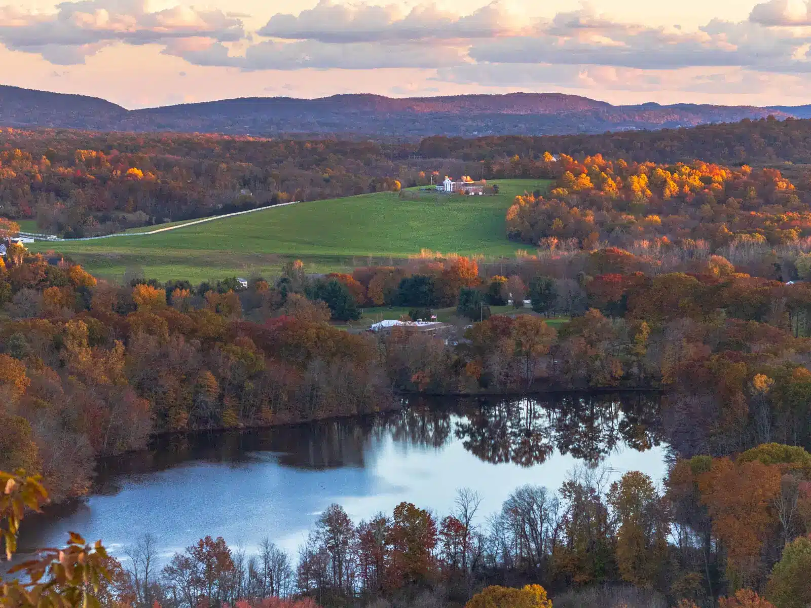 fall view from hike atop ragged mountain in Berlin with green field in distance, pond below and fall colored leaves all around.