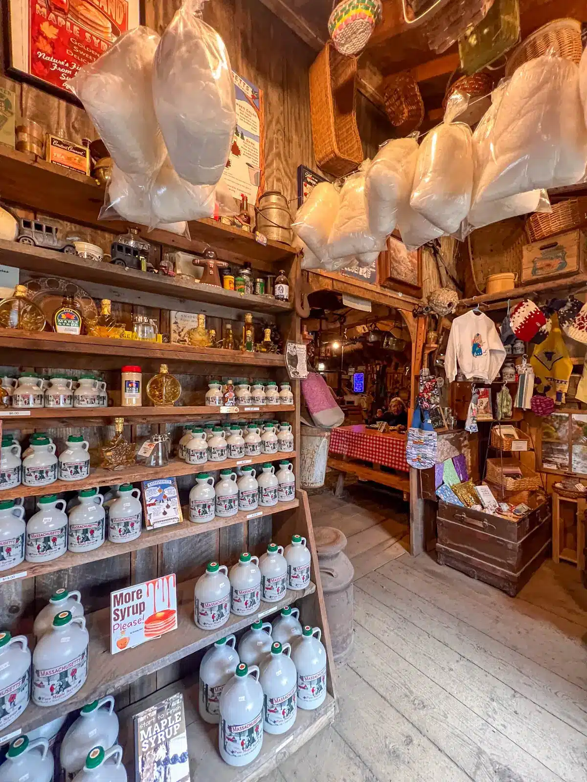 inside high hopes maple house in massachusetts with a wall of maple syrup jugs on wooden shelves and cotton candy hanging from ceiling above.