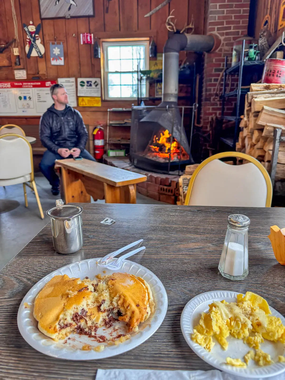 inside maple corner farm in granville with wooden table and breakfast on it and small fireplace.