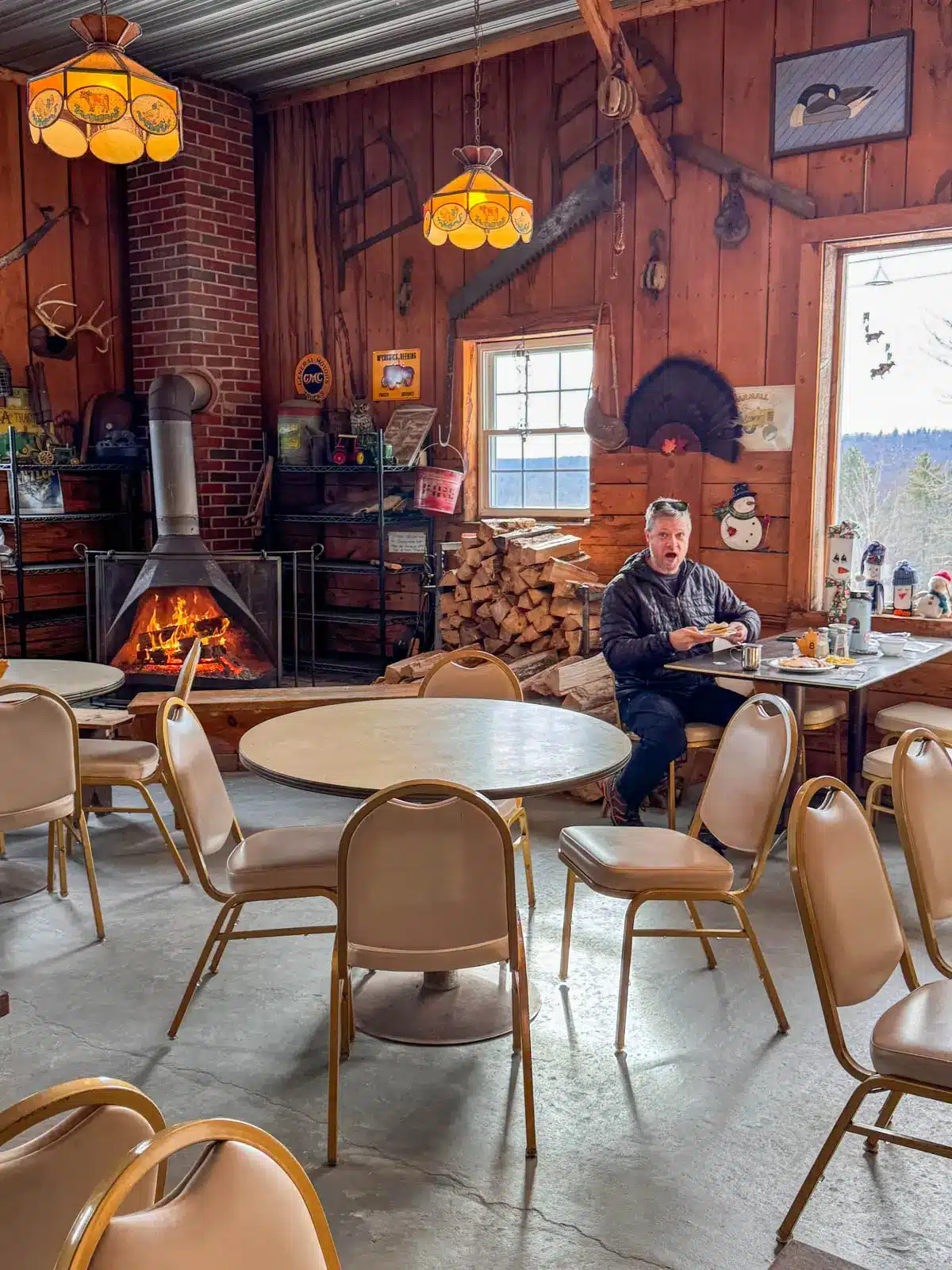 inside maple corner farm with tables and chairs and fireplace lit in corner of the room.