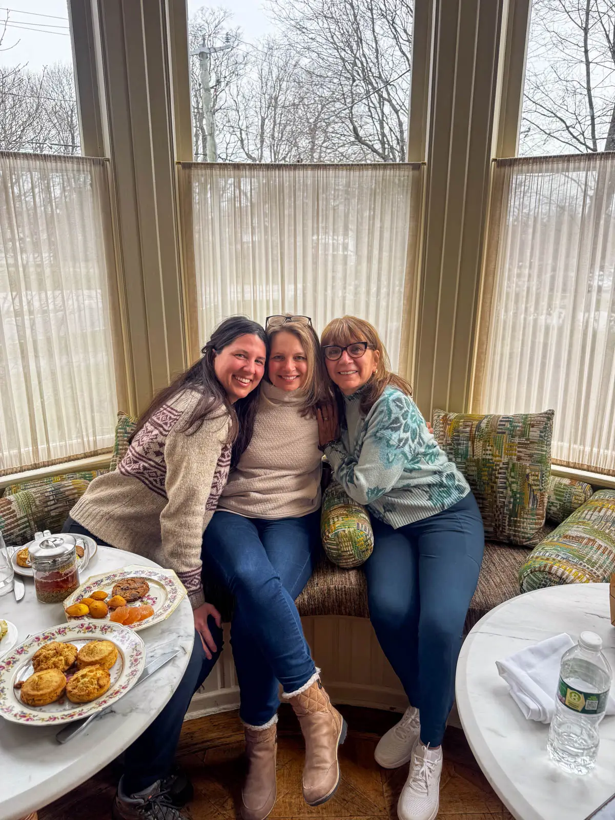 a mother and two daughters smiling and sitting on a couch behind a white table for afternoon tea in litchfield ct.