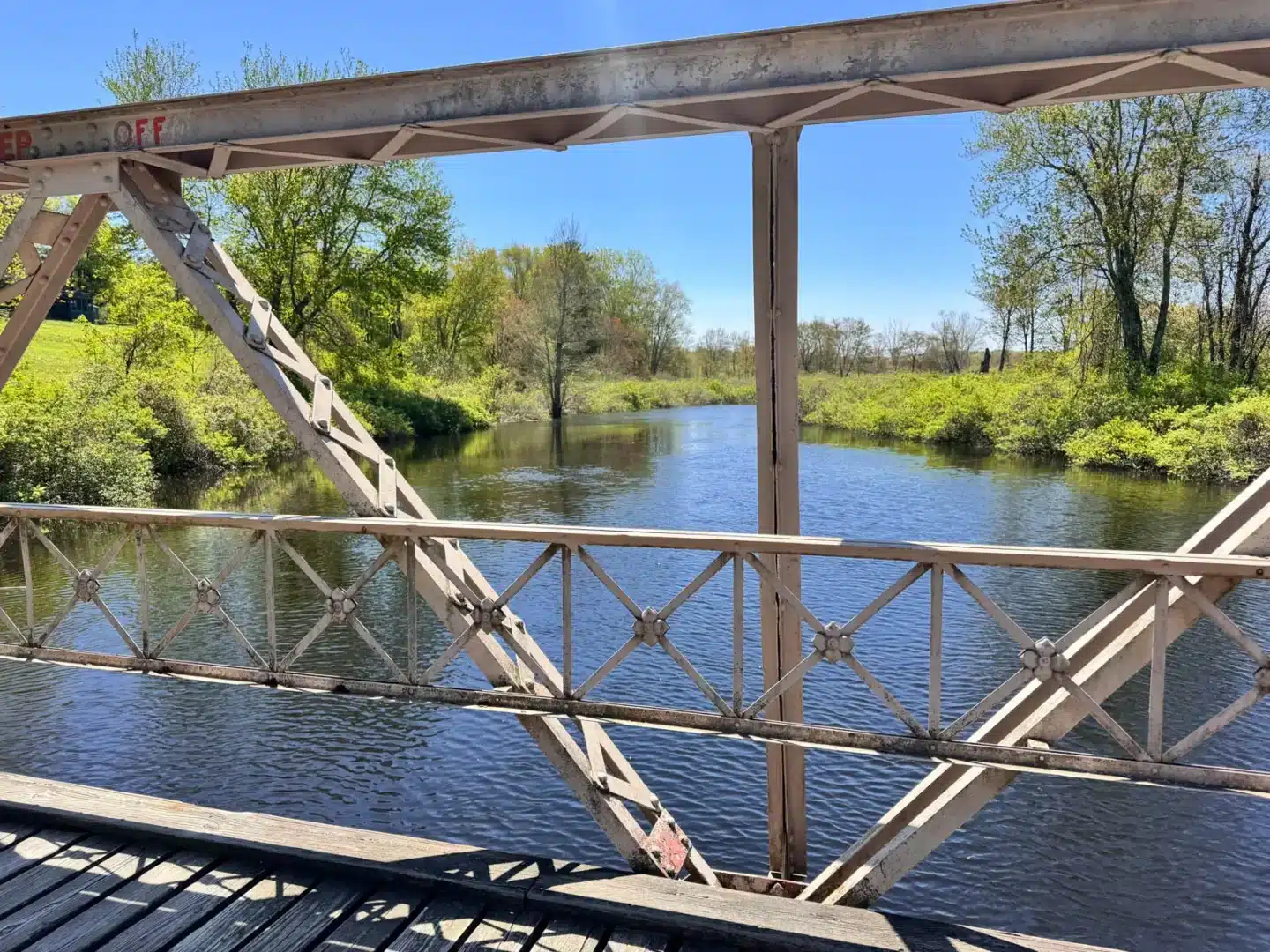 an old iron bridge crossing over bright green river lined with bright green grass and trees on a spring day in litchfield.