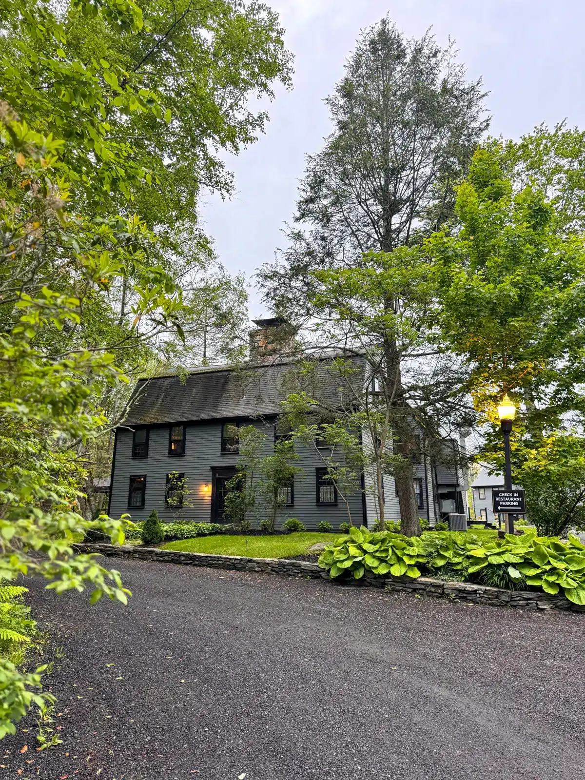 driveway entrance to the lost fox inn in litchfield with stone pillar and dark gray colonial in background surrounded by fresh greenery in spring.