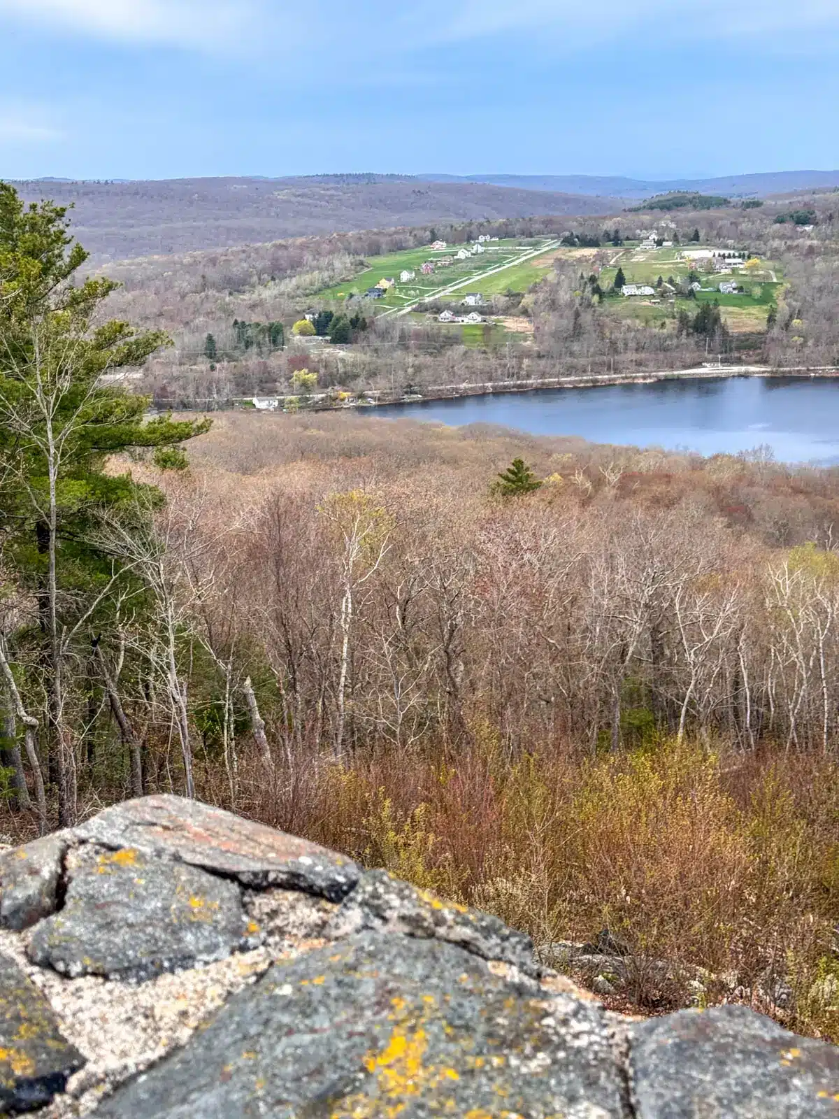view from top of stone mount tom tower in litchfield with blue body of water in distance and some bare trees and some green fields.