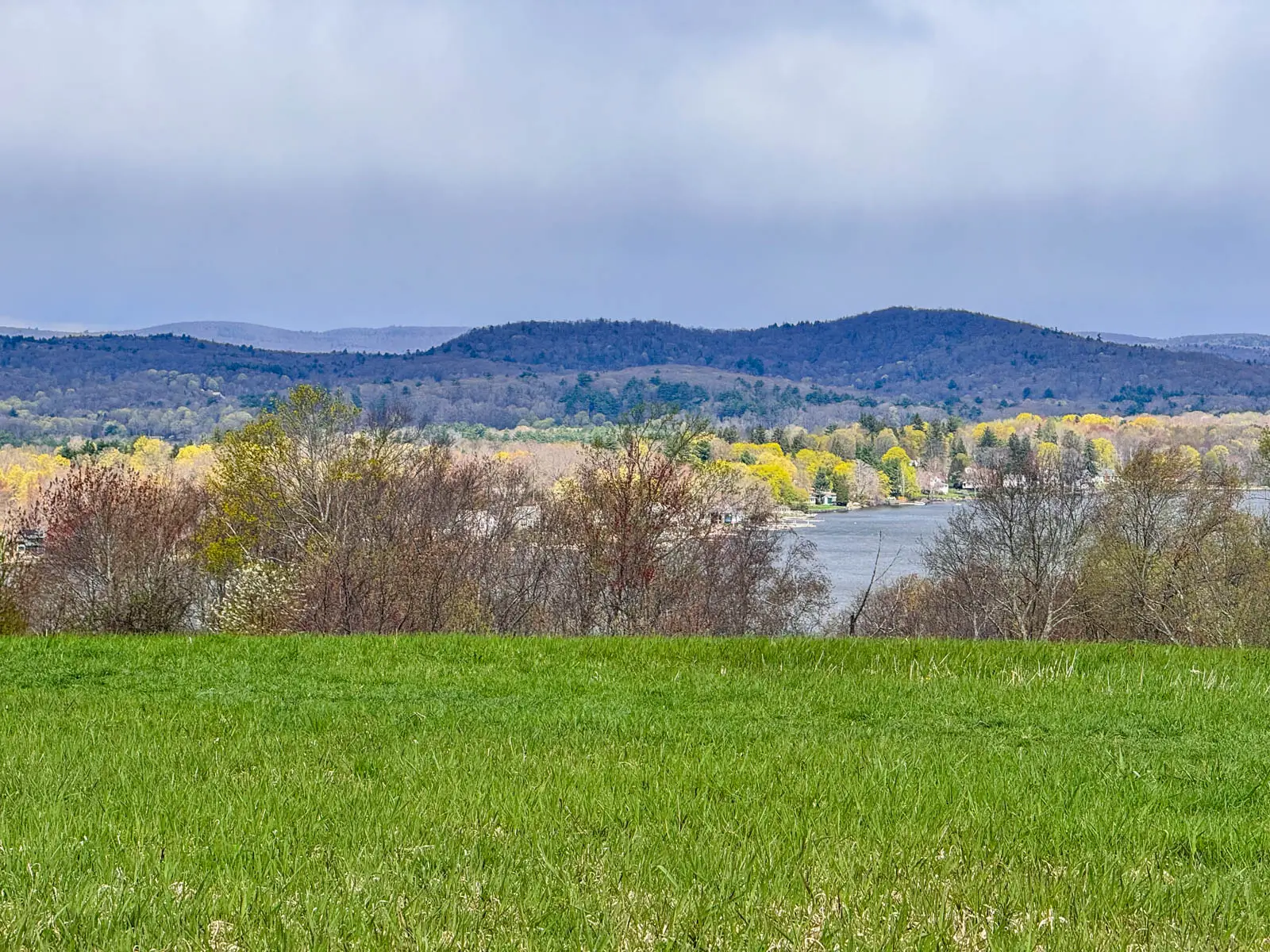 view of green lawn, body of water, and then rolling hills in distance from a hike at white memorial in litchfield.