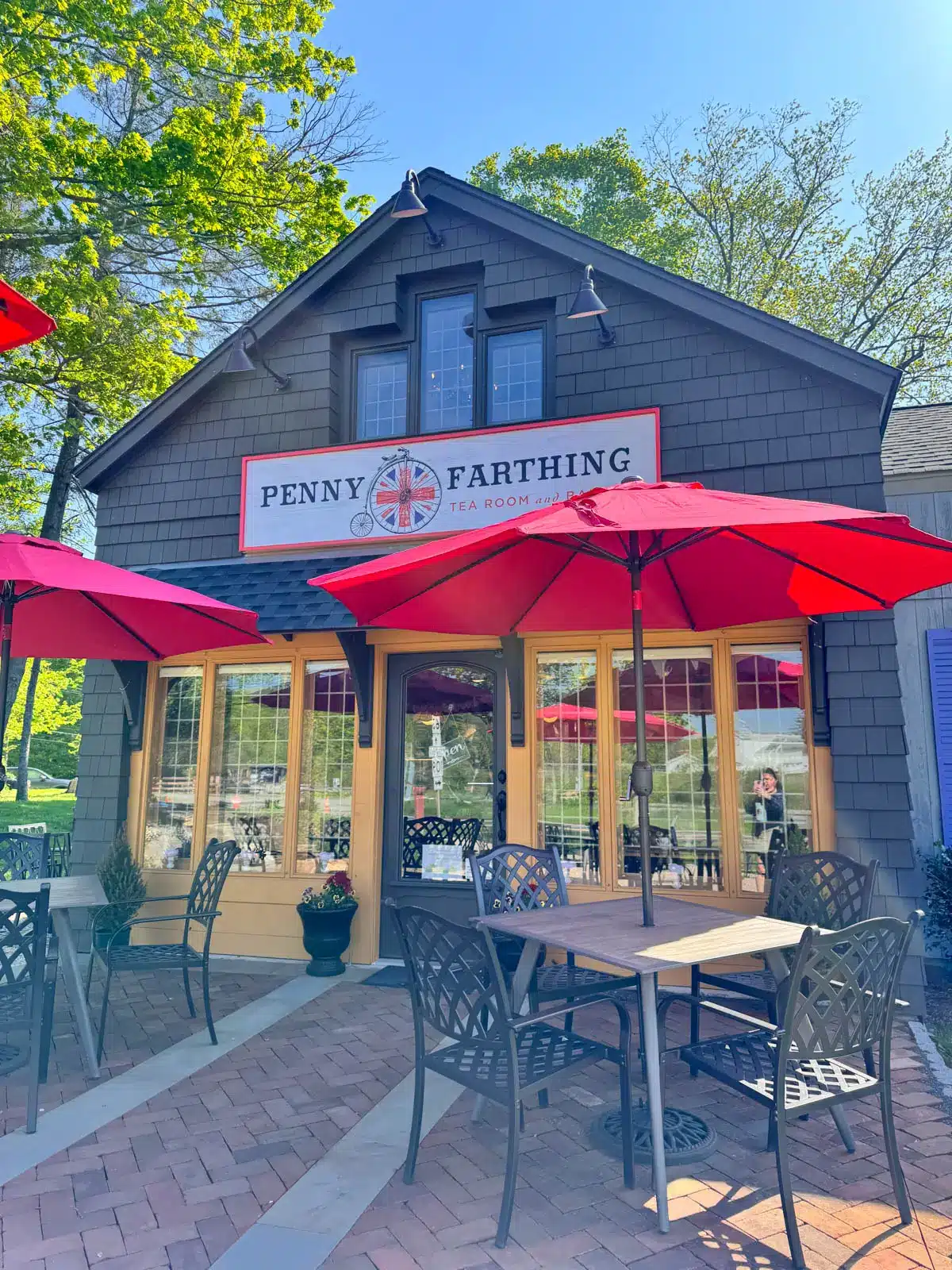 outside of penny farthing tea room in litchfield with two wooden tables outside with red umbrellas on bright sunny day.