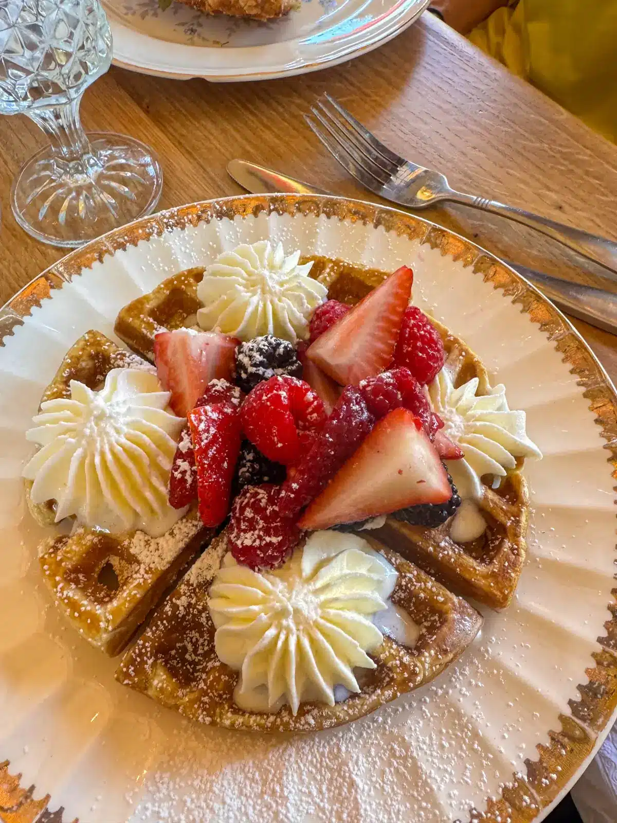 white plate with belgian waffles, strawberries, and whipped cream.