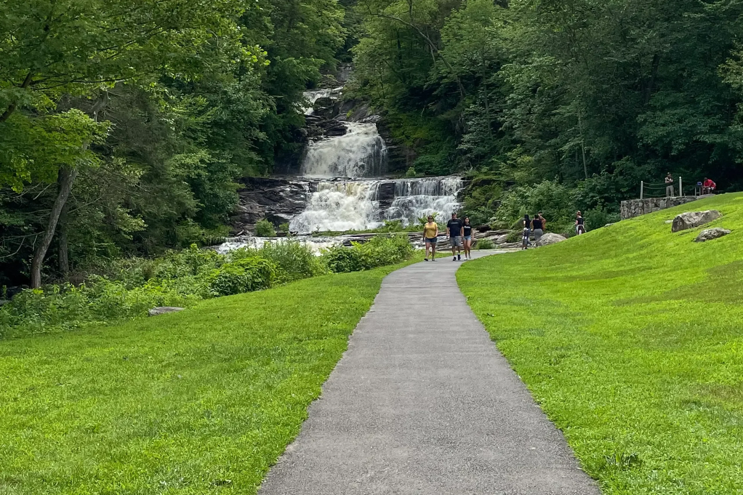 kent falls from a distance with green lawn all around and paved path