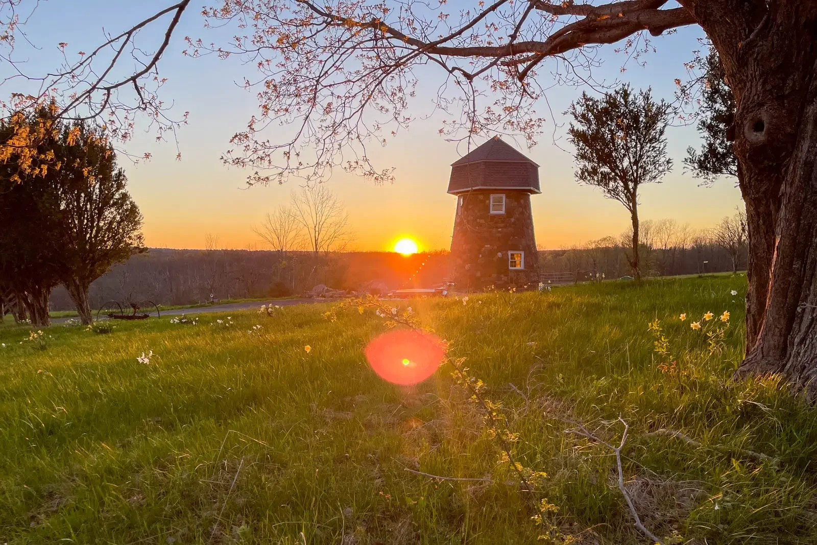 sunset view of small windmill building on green grass and orange sun setting in distance in litchfield connecticut.
