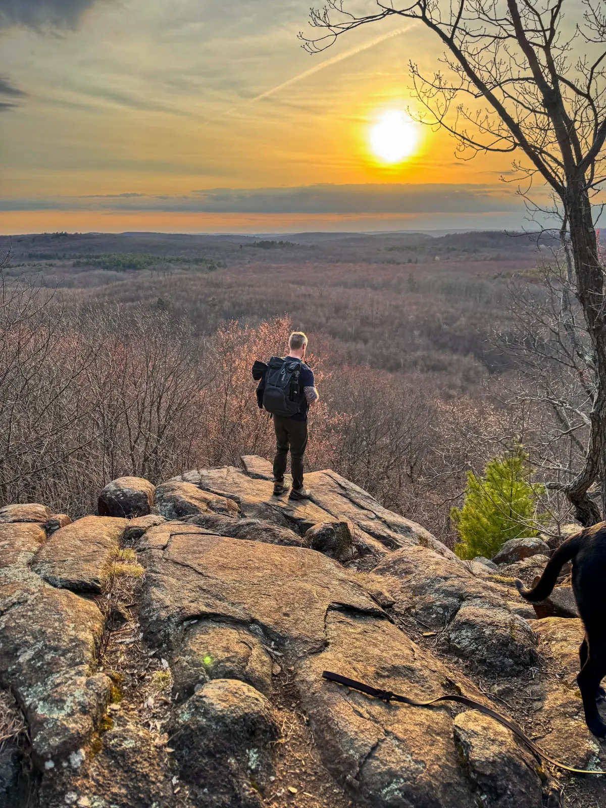 sunset view from top of hike in connecticut with golden sun setting and man standing on cliff ledge.