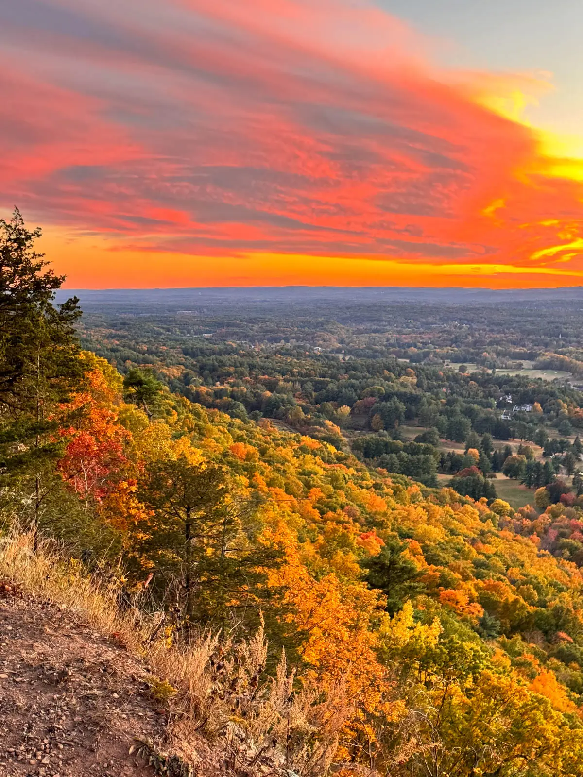 view from talcott Mountain at sunset time with swirly bright pink clouds in sky and sea of autumn colored leaves below.