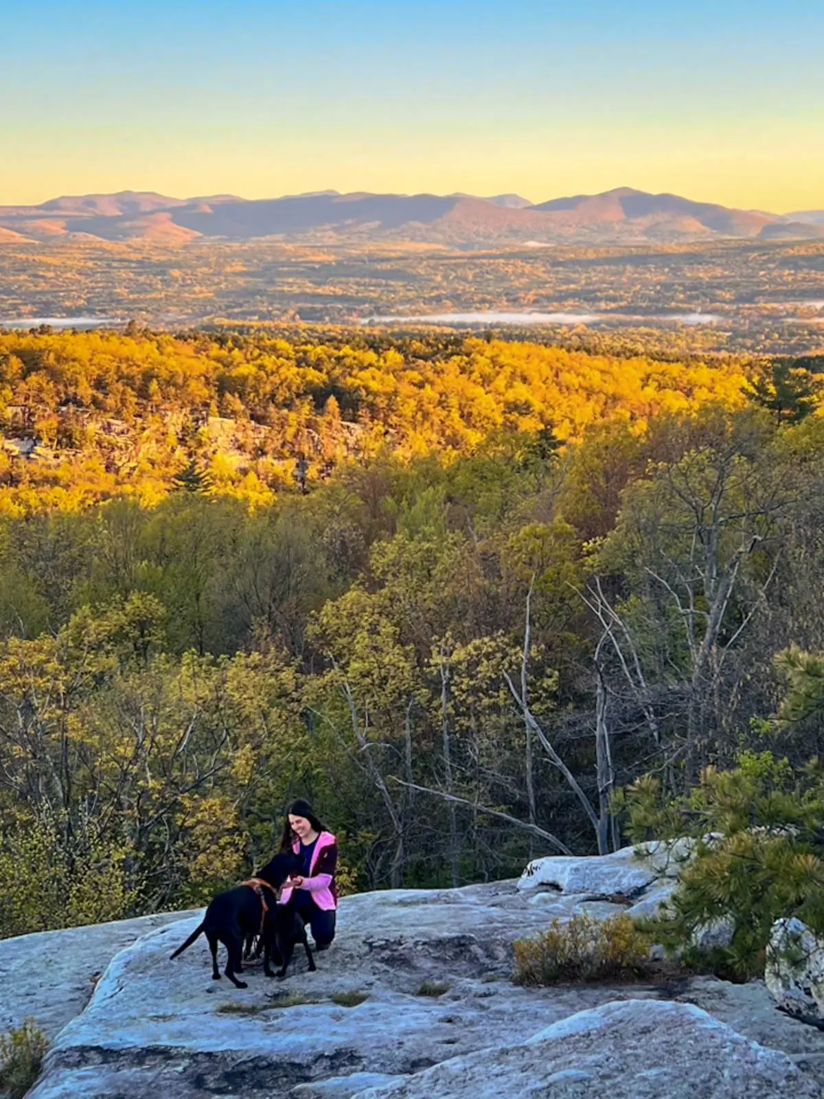 woman on top of mountain cliff with rolling mountains behind her at sunrise time in minnewaska state park.