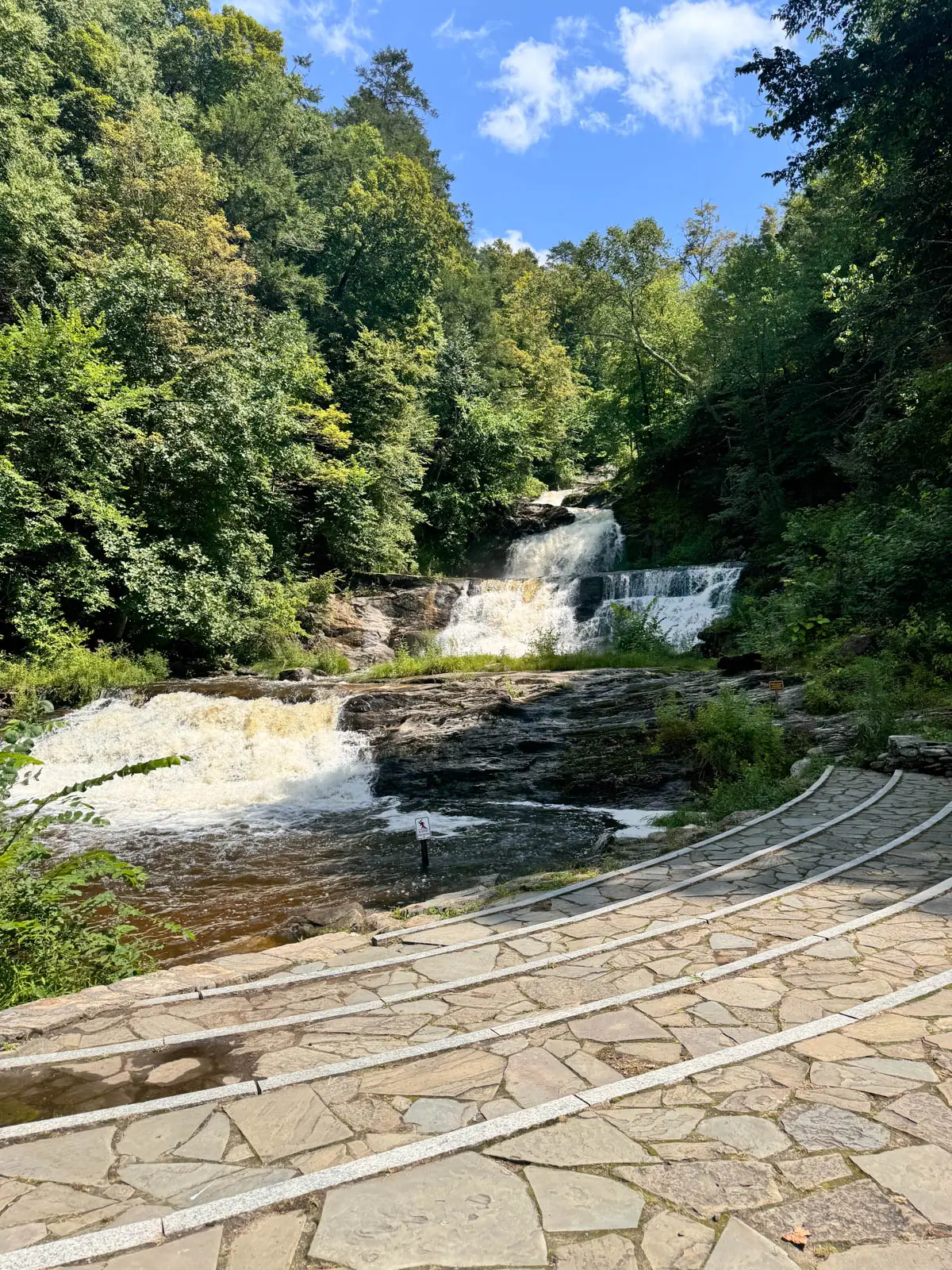 multi-tiered waterfall in kent connecticut surrounded by green trees and a blue sky above.
