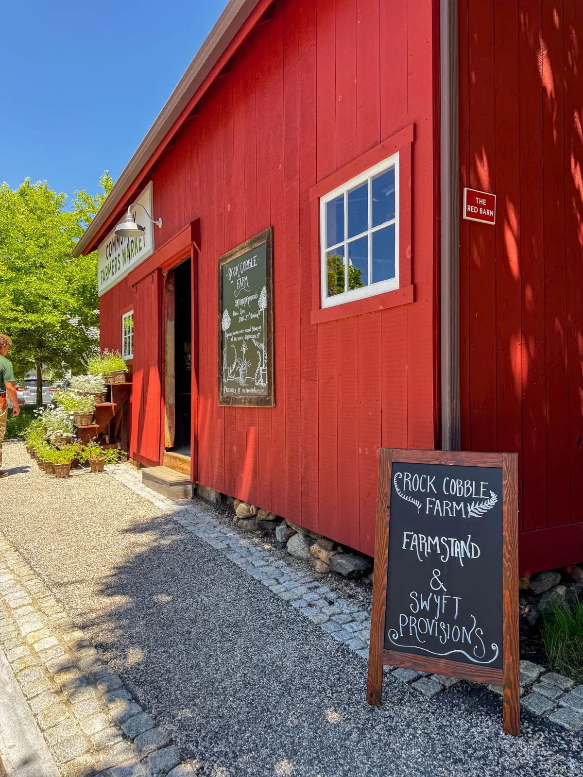 bright red barn in kent connecticut with a chalkboard out front with writing about the farm items sold inside.