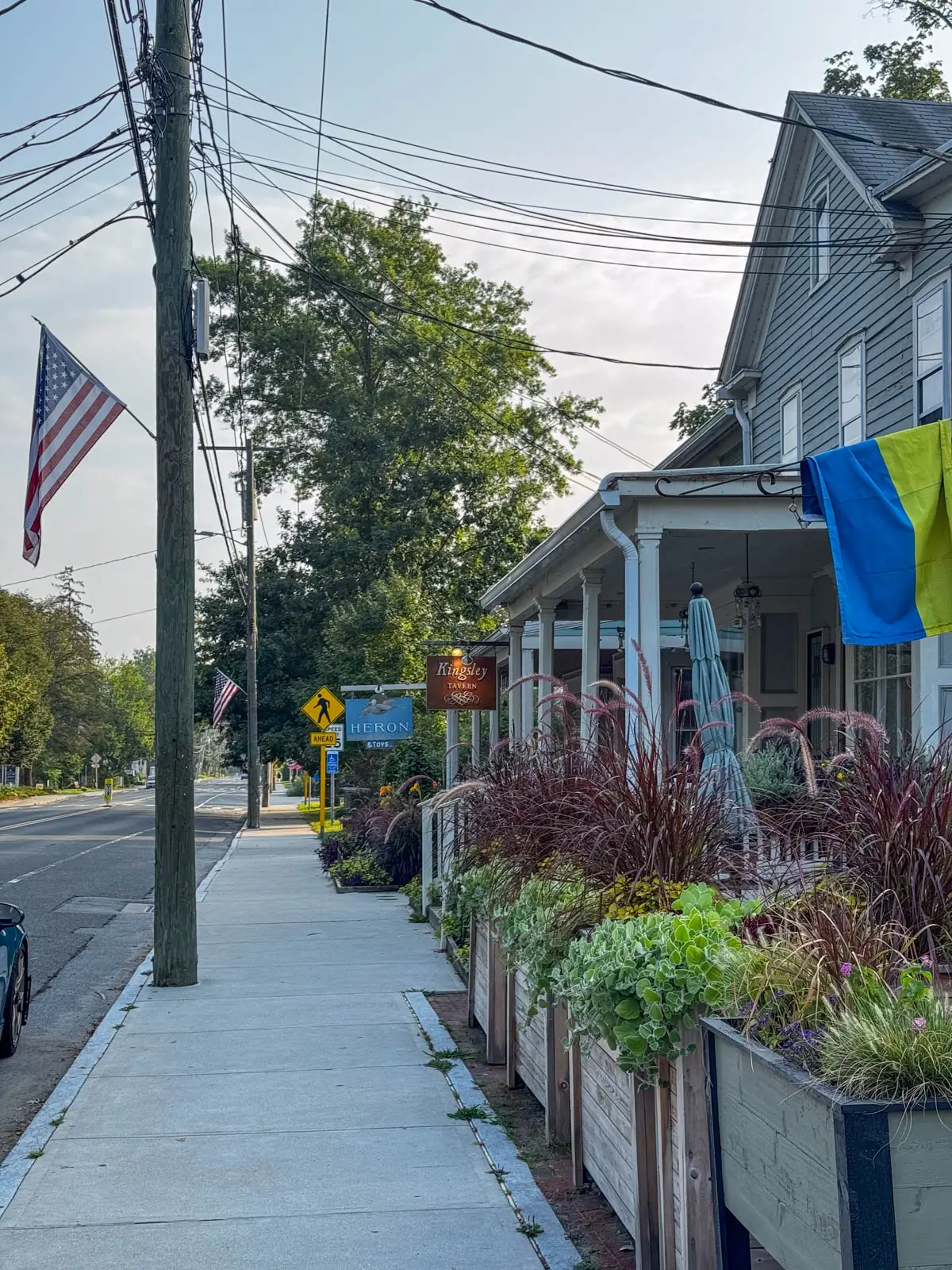 sidewalk in downtown kent ct with a big white porch and american flag sticking out.