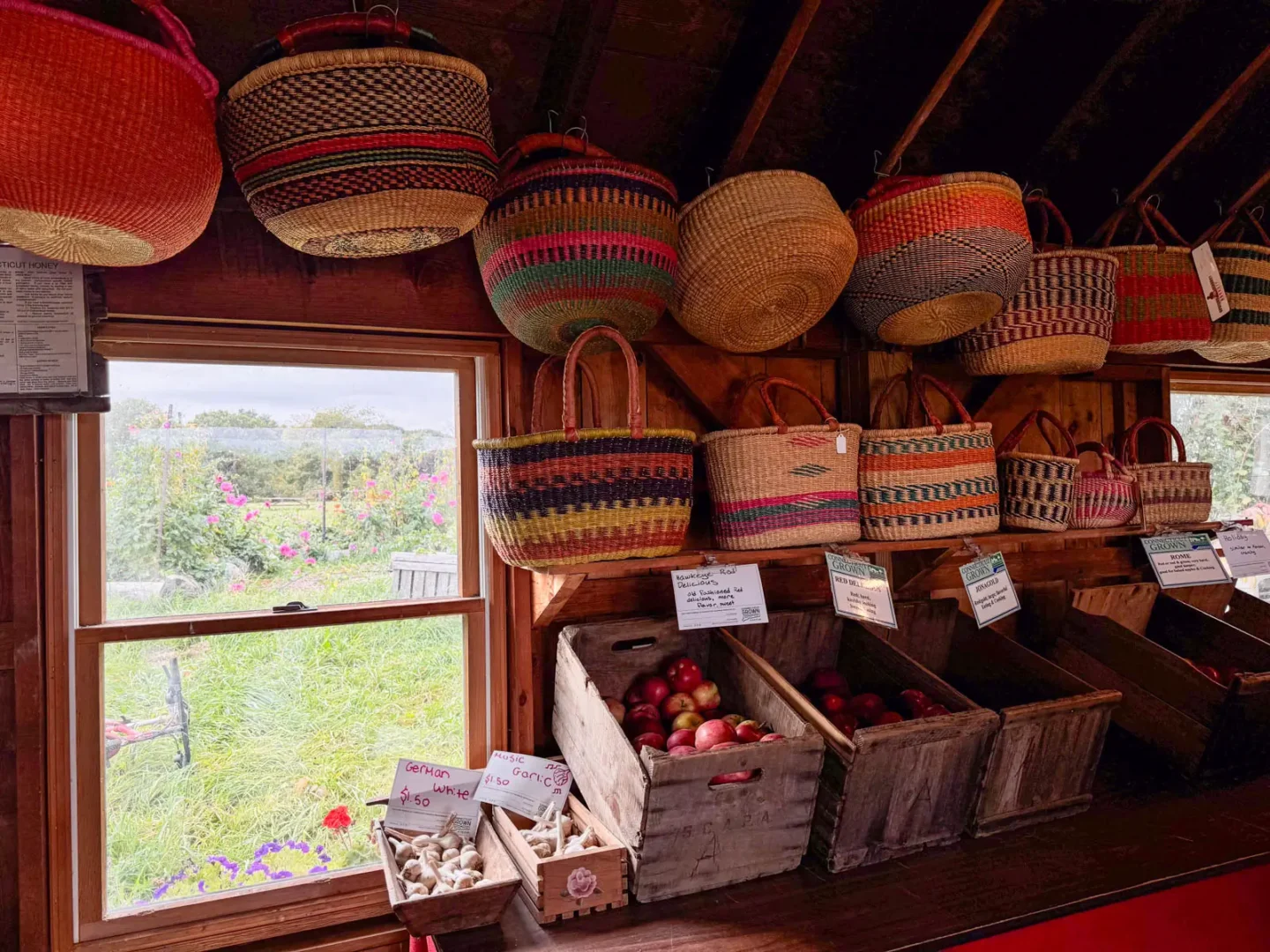 woven baskets hanging from a wall inside a barn and buckets of apples for sale.