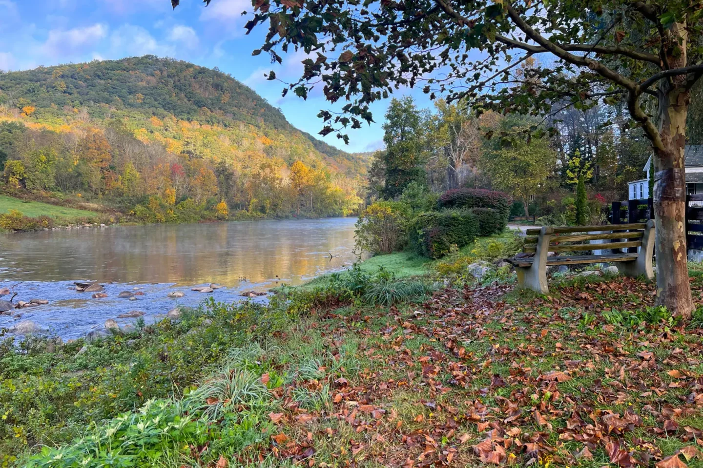 fall view of housatonic river with rolling hill in distance and orange, red, and yellow leaves on ground in front of river.