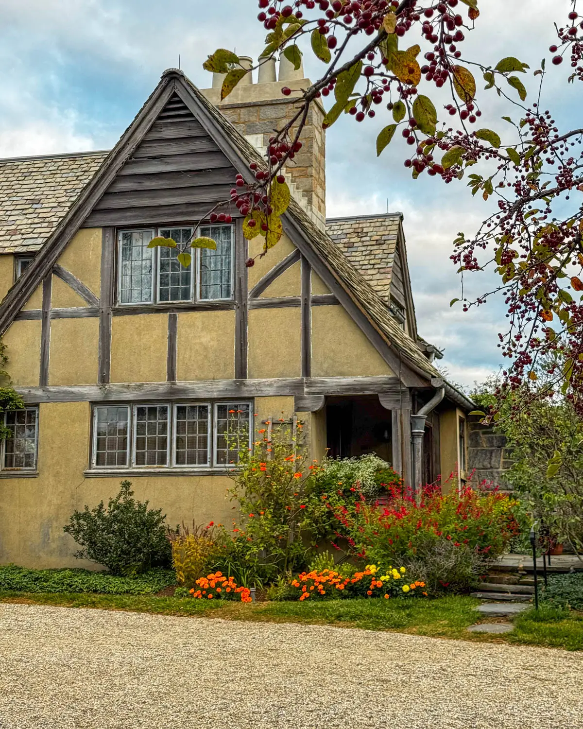 english tudor at topsmead state park in litchfield connecticut in fall with mums in front of mansion and fall colored leaves framing the photo.