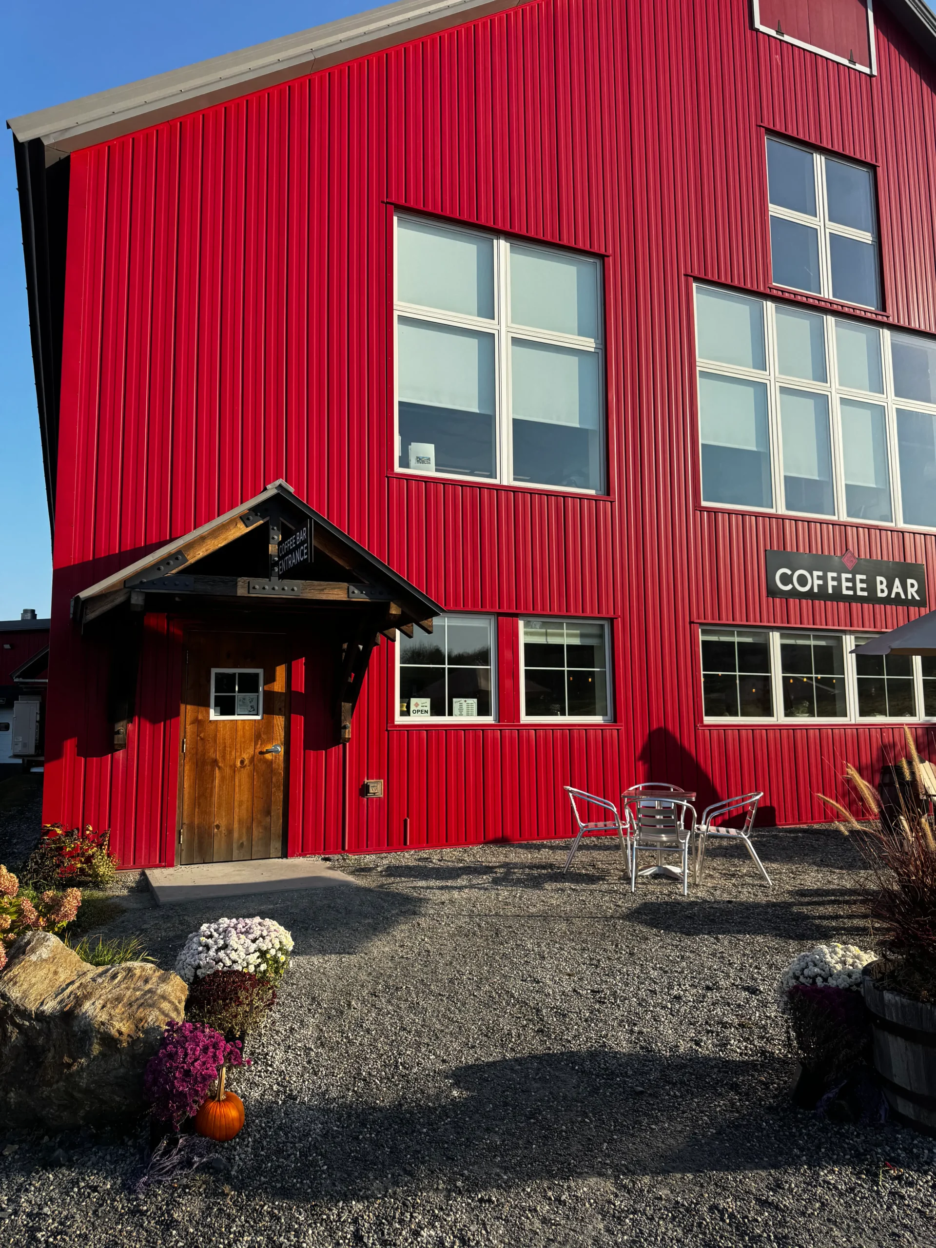 big red barn with a black sign with light letters that says "coffee bar" and a few mums in from by the wooden door.