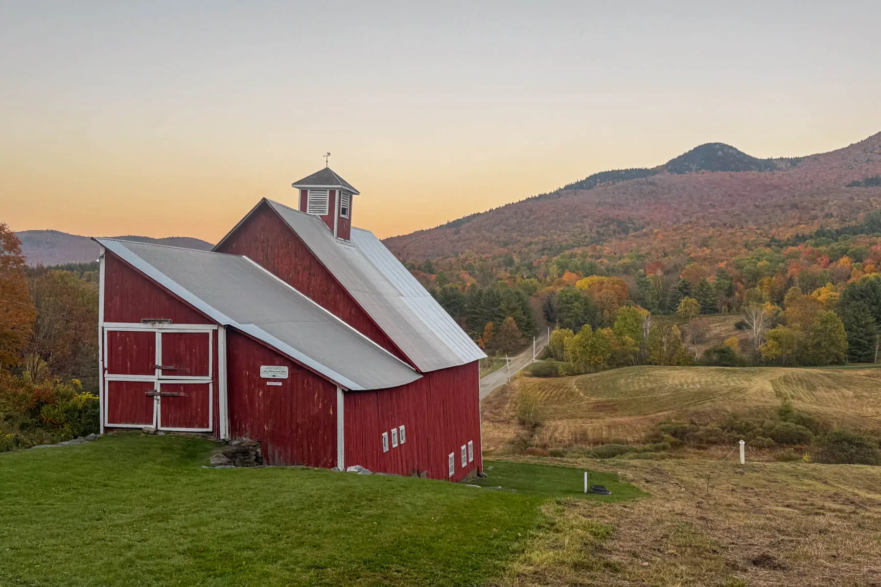 big red barn at sunset time in stowe vermont with orange colored mountain range behind it in fall.