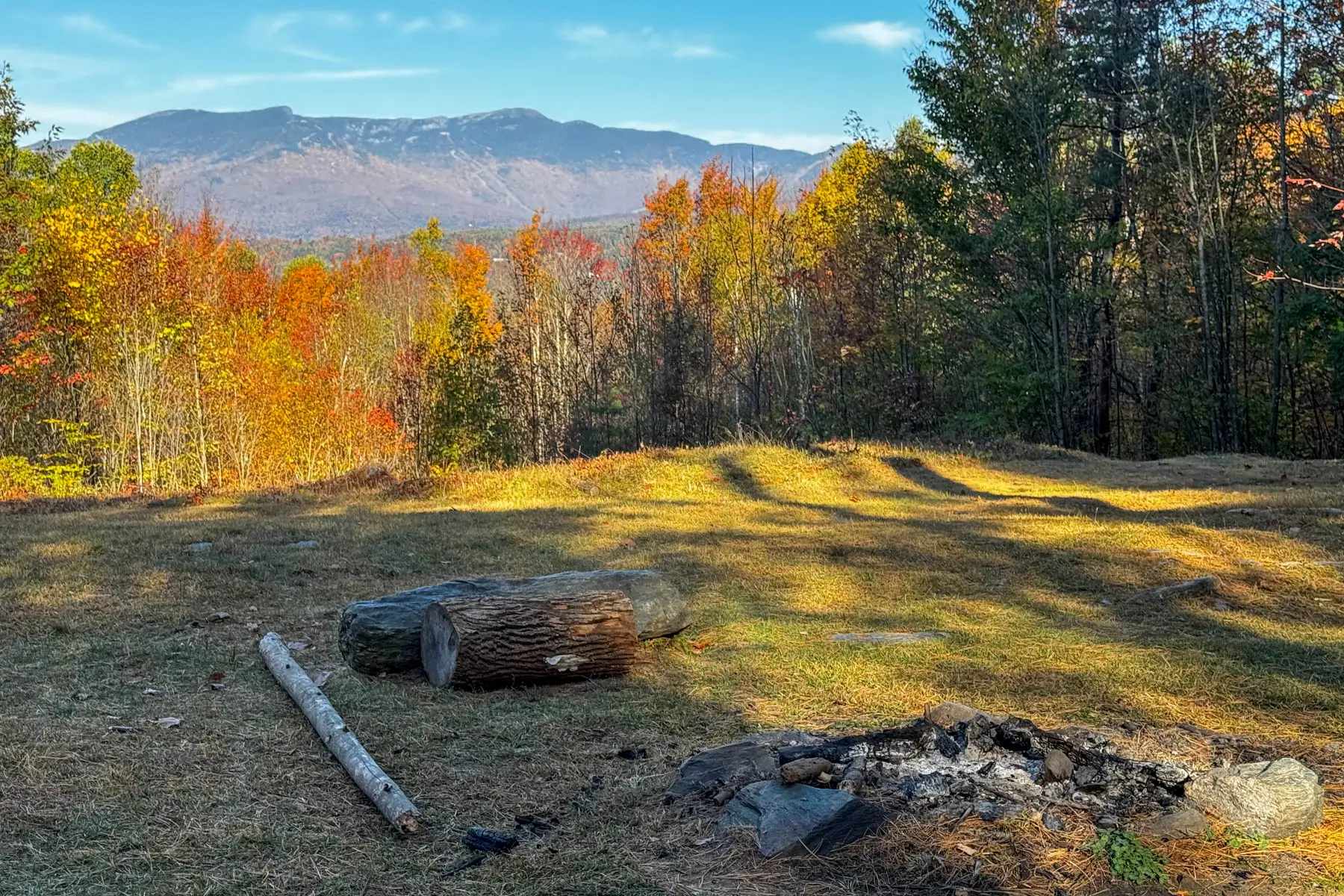 view of open meadow at sunrise time with soft golden sky on a hike in fall in stowe with hills of orange, red, and green trees and rolling hills and big mountain in distance.
